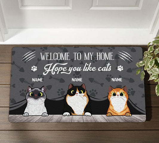 Doormat with three cartoon cats and text 'Welcome to my home, hope you like cats' on a wooden floor.