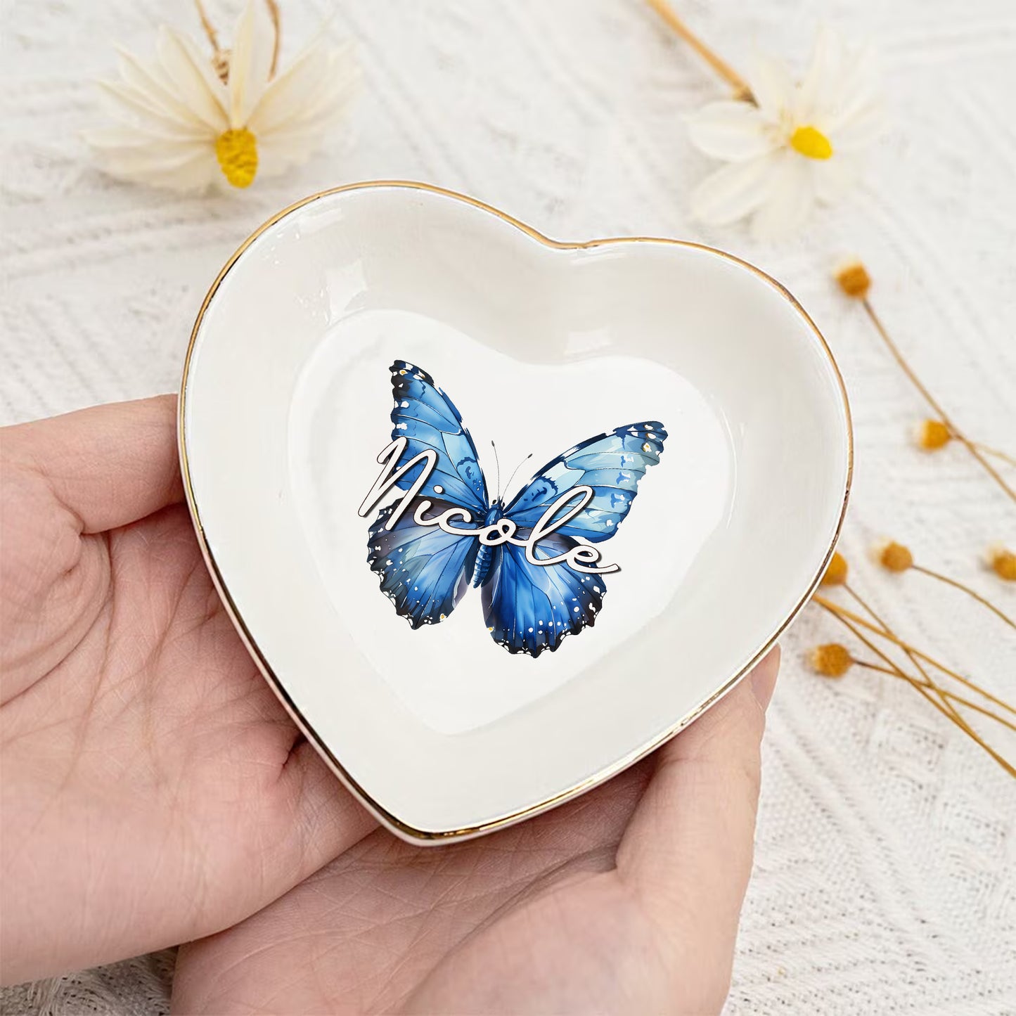 Heart-shaped trinket dish with a blue butterfly and 'Nicole' text, held in a hand with a light background.